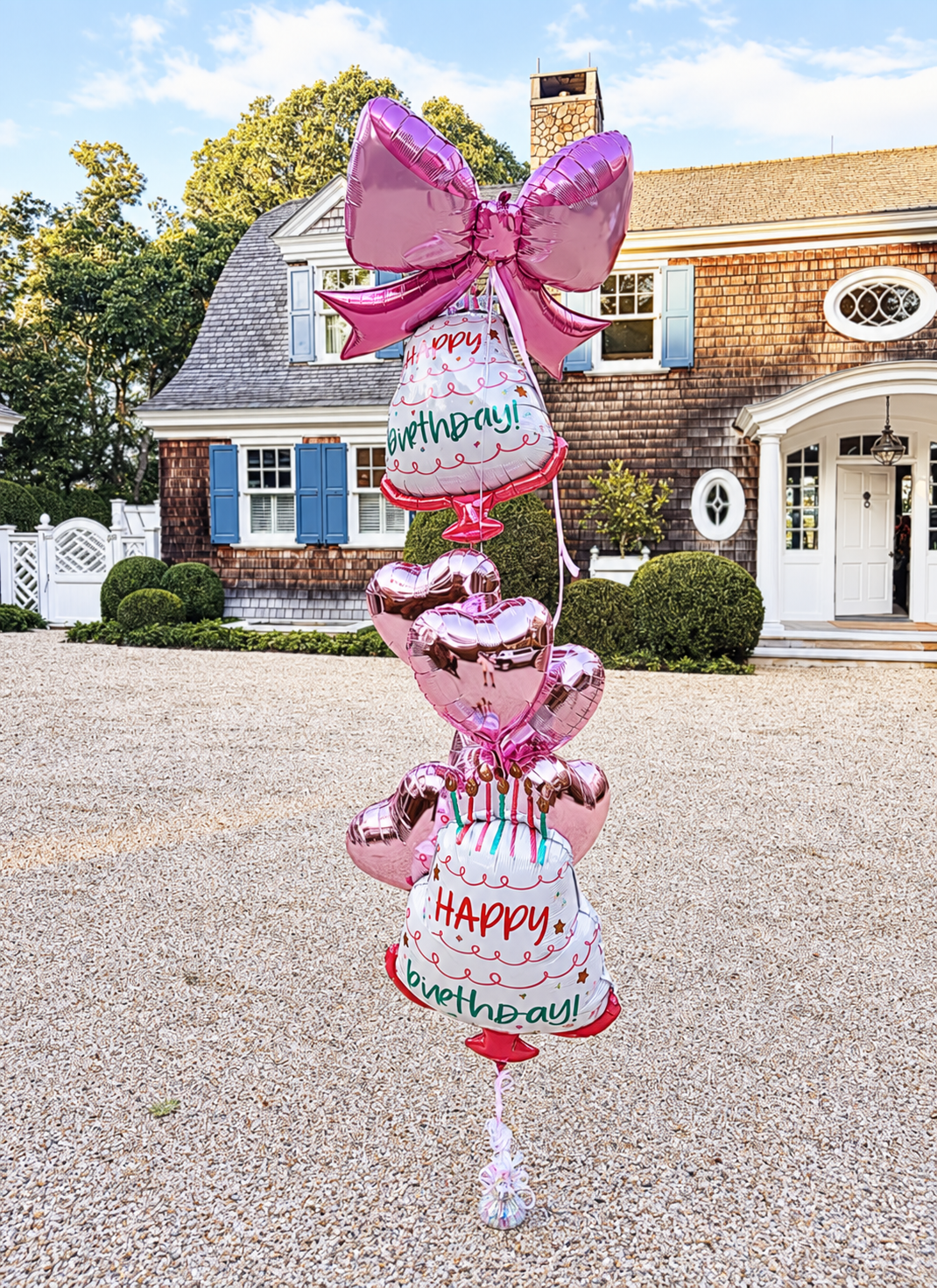 A pink birthday balloon arrangement with a large bow, heart balloons and cake balloons delivered to a Hamptons home