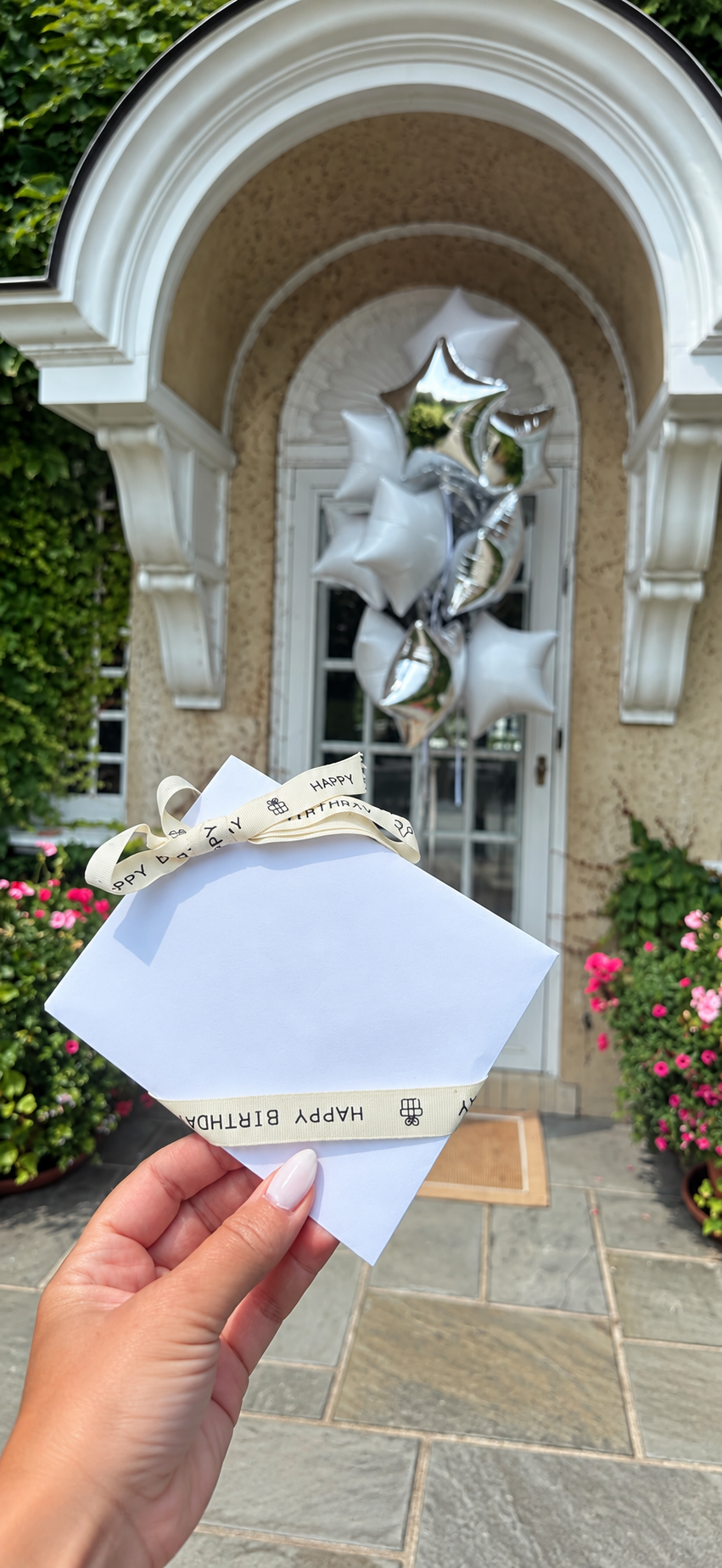 A pale-blue birthday card and white and silver star balloon delivery at an arched Hamptons doorway